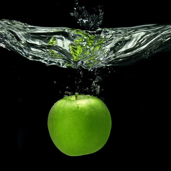 Green apple dropped into water with splash isolated on black