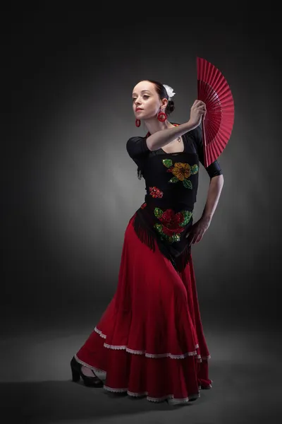 Young woman dancing flamenco with fan on black