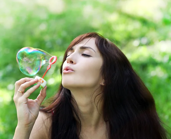 Adorable young girl inflating colorful soap bubbles in summer pa