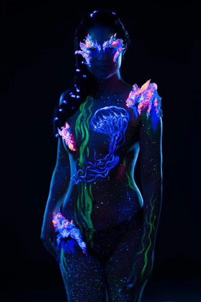 Beautiful woman with body art glowing in ultraviolet light