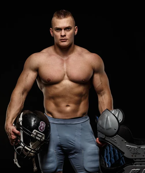 Man with naked muscular torso holding american football player accessories