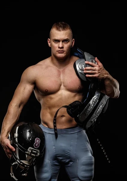 Man with naked muscular torso holding american football player accessories