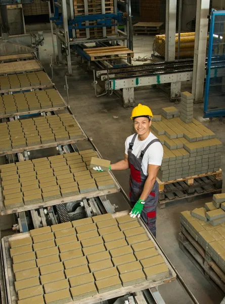 Young worker near conveyor belt with paving stone on a factory