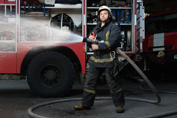 Firefighter holding water hose near truck with equipment