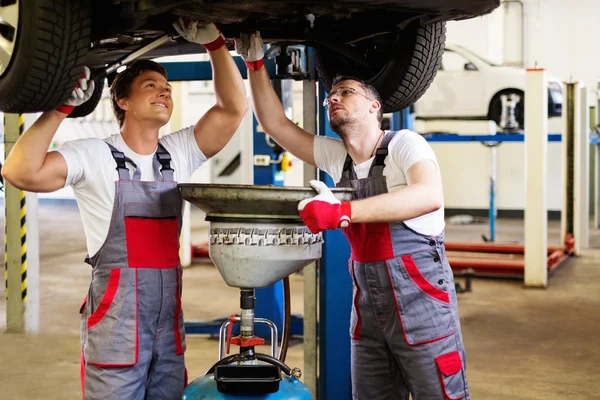 Two mechanic changing oil in a car workshop