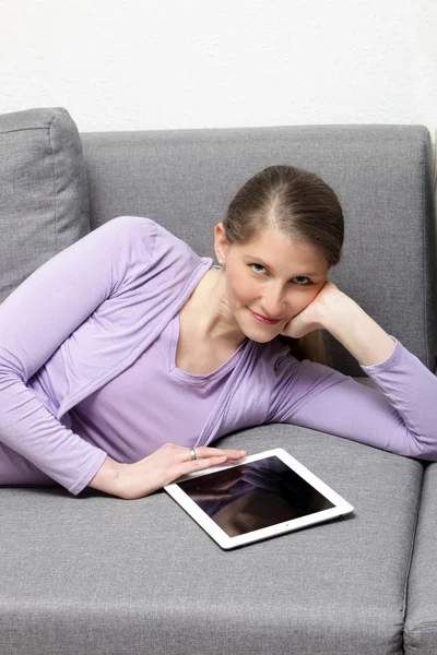 Lying woman on brown couch browsing using her ipad