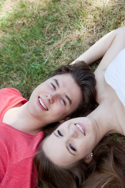 Two teenagers lying head to head on grass