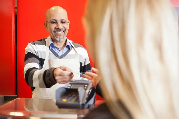 Mature Man Accepting Credit Card From Young Woman At Supermarket