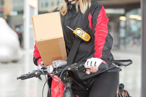 Female Cyclist With Cardboard Box And Courier Bag On Street