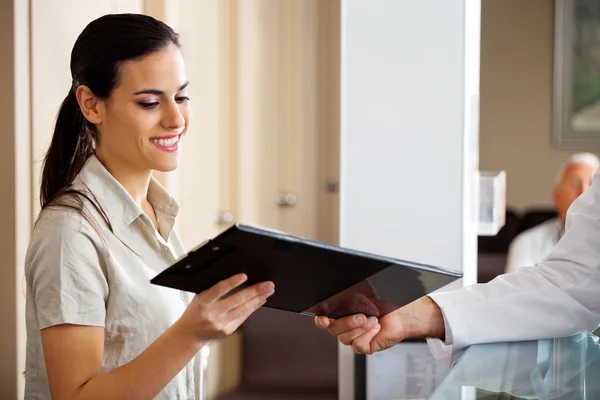 Receptionist Taking Clipboard From Doctor