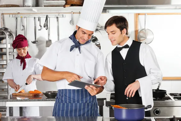 Waiter And Chef Using Digital Tablet In Kitchen