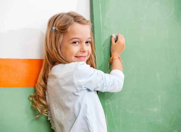 Girl Writing On Green Chalkboard In Classroom