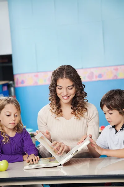 Young Teacher And Children Reading Book In Classroom