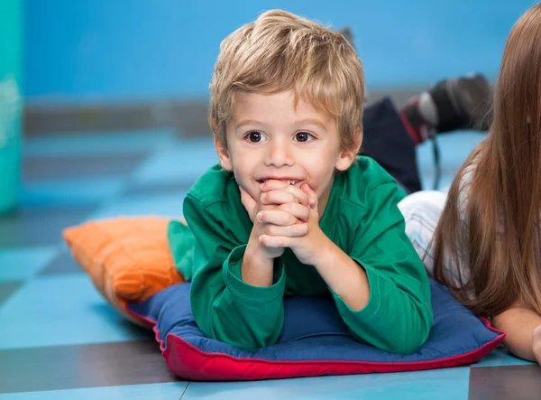 Boy With Hands Clasped Lying On Floor In Kindergarten