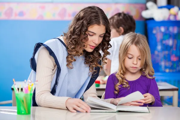 Teacher And Little Girl Reading Book In Classroom