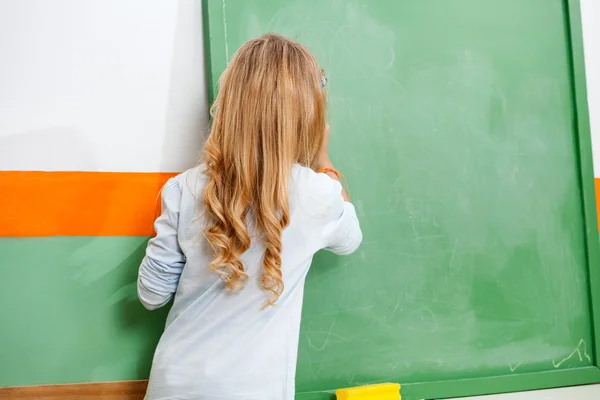 Little Girl Writing On Chalkboard In Classroom