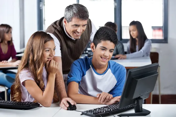 Happy Mature Teacher And Students Using Computer