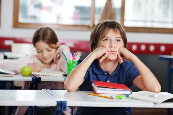 Bored Schoolboy Looking Away Sitting At Desk In Classroom