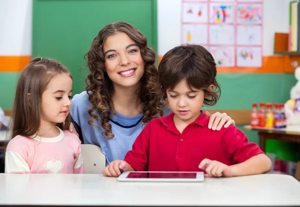 Teacher With Children Using Digital Tablet At Desk