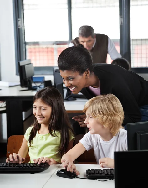 Teacher Assisting Schoolchildren In Using Desktop Pc