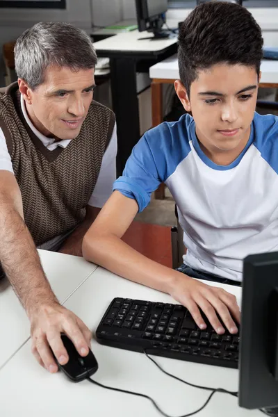 Teacher With Male Student Using Computer At Desk