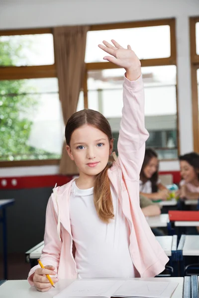 Schoolgirl Raising Hand While Standing In Classroom