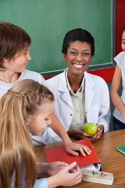 Teacher Holding Apple With Students Standing At Desk