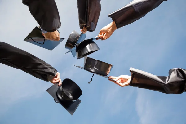 Students Raising Mortar Boards Against Sky On Graduation Day