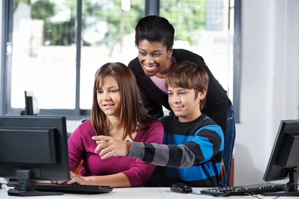 Teacher Assisting Teenage Students In Computer Lab