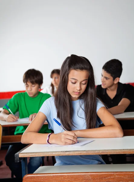 Female Student Writing Paper At Desk In Examination