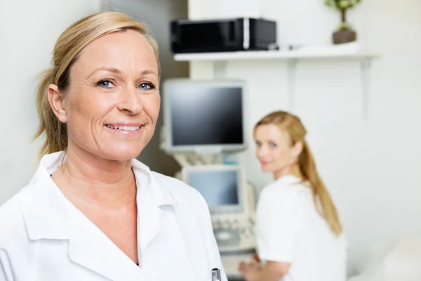 Female Doctor Smiling With Colleague In Background