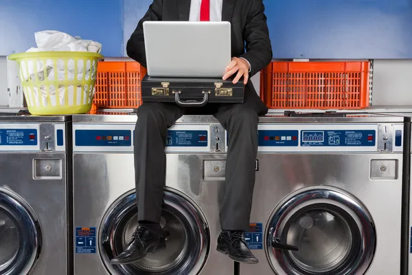 Businessman Using Laptop While Sitting On Washing Machine