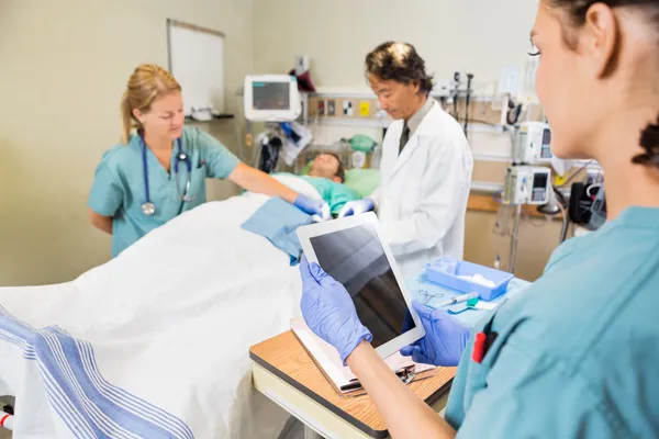 Nurse Holding Digital Tablet While Colleague And Doctor Operatin