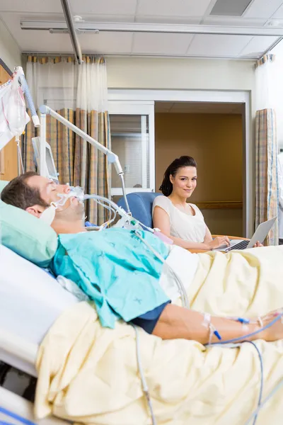 Woman With Laptop Sitting By Patient In Hospital