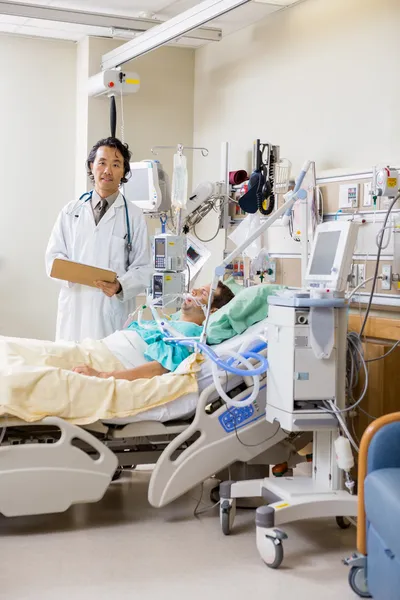 Doctor With Patient's Report Standing By Bed