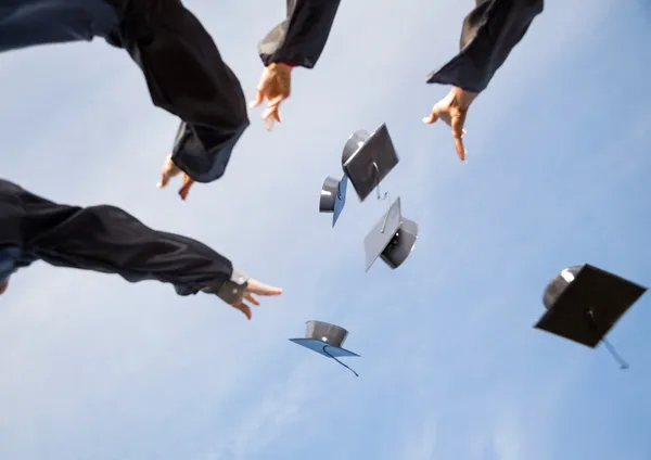 Students Throwing Mortar Boards In Air Against Sky