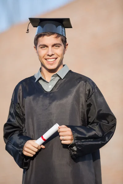 Happy Man In Graduation Gown Holding Certificate On Campus