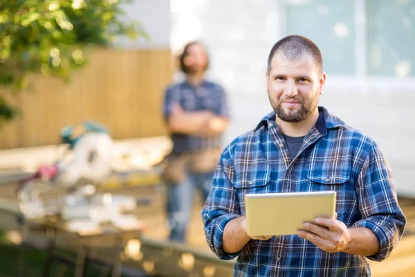 Manual Worker Holding Digital Tablet With Coworker Standing In B
