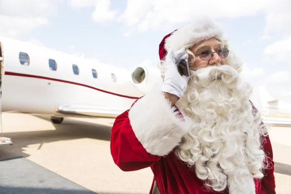 Santa Claus Communicating On Mobile Phone Against Private Jet