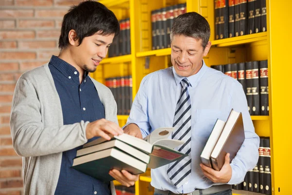 Student Holding Books While Discussing With Librarian In Library
