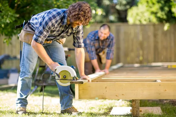 Carpenter Cutting Wood With Handheld Saw While Coworker Helping