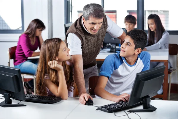 Teacher Using Computer With Students In Classroom