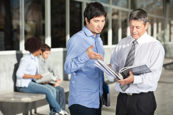 Teacher Holding Books While Discussing With Student On Campus