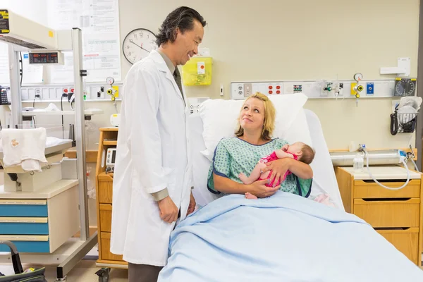 Mother Holding Newborn Babygirl While Looking At Doctor
