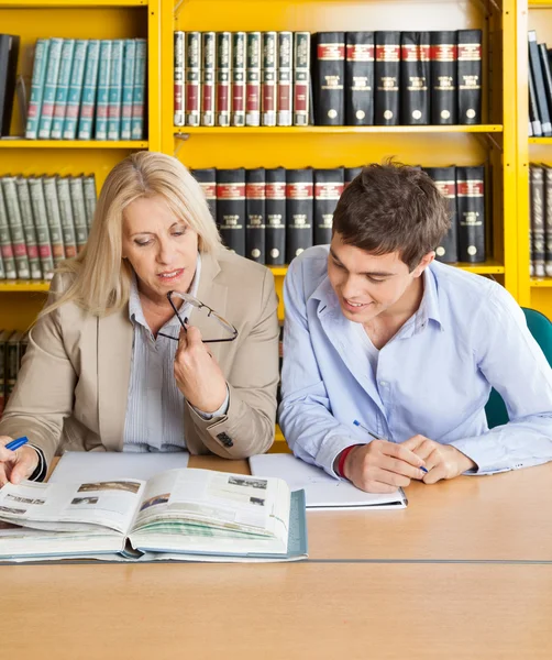Teacher And Student Looking At Book While Sitting In Library