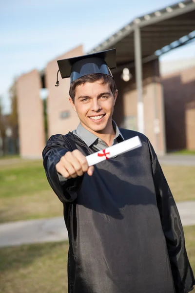 Man In Graduation Gown Showing Diploma On University Campus