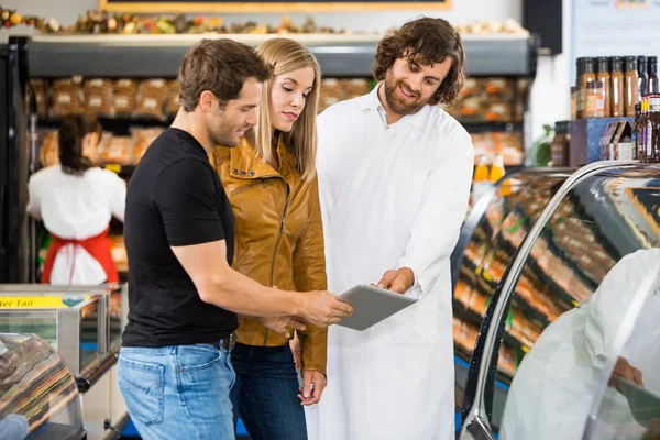 Salesman And Couple Using Digital Tablet At Butcher\'s Shop