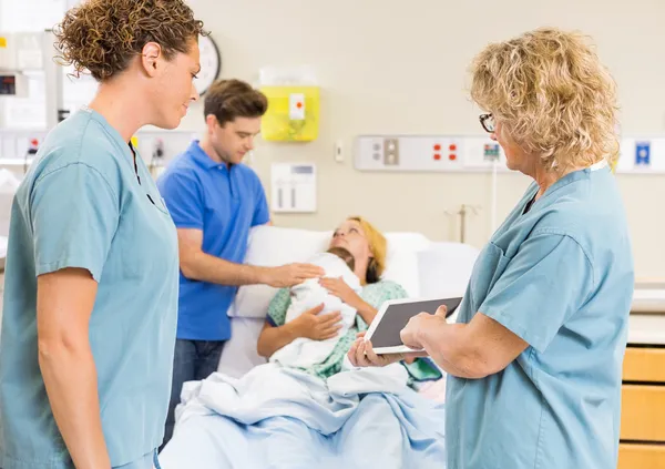 Nurses Discussing Report On Digital Tablet Against Couple With B