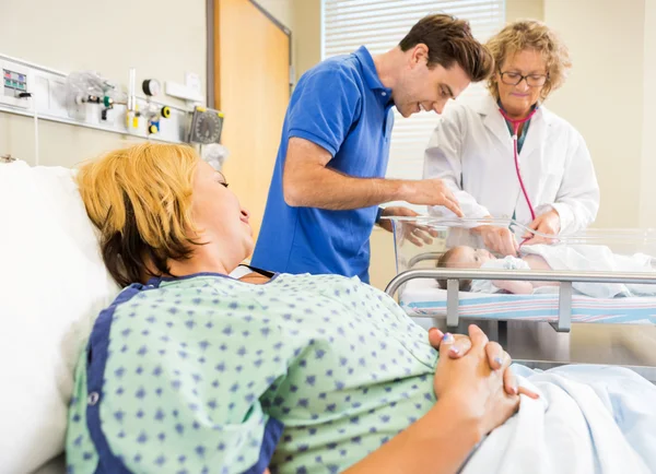 Mature Doctor Examining Newborn Babygirl While Parents Looking A