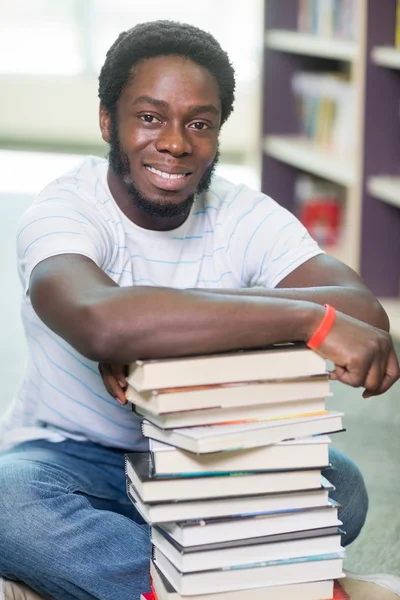 Smiling Student With Stacked Books Sitting In Library